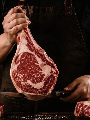 Talhante a segurar um tomahawk maturado, com cortes de carne na bancada